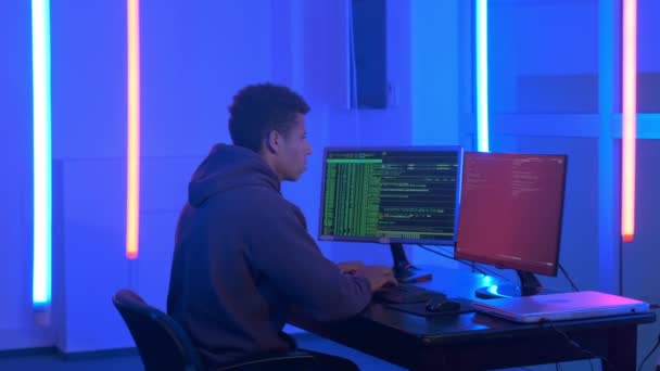 Fotografía mediana del joven africano escribiendo programas de hackers en cuarto oscuro con luces de neón — Vídeo de stock