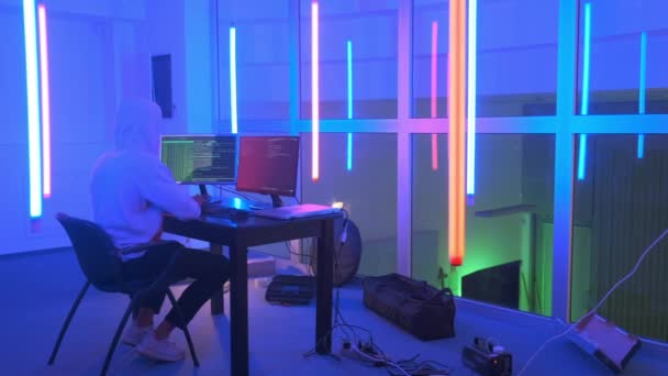 Lugar de trabajo del hacker: hacker trabajando en una habitación con luces de neón de colores — Vídeos de Stock