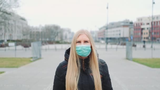 Пандемия коронавируса: блондинка в медицинской маске идет по улице — стоковое видео