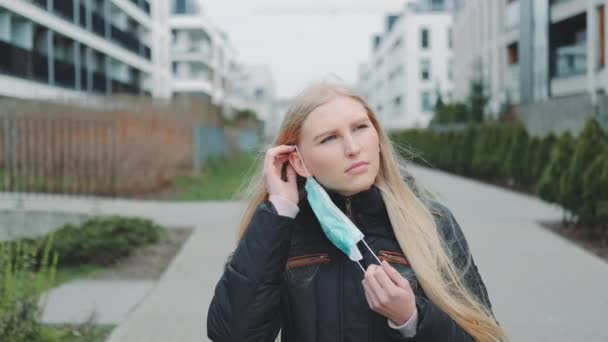 Женщина надевает медицинскую маску, выходя на улицу — стоковое видео