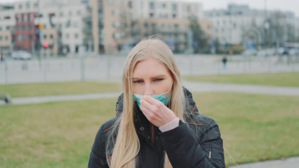 Jonge vrouw zet een medisch masker op haar gezicht op straat — Stockvideo