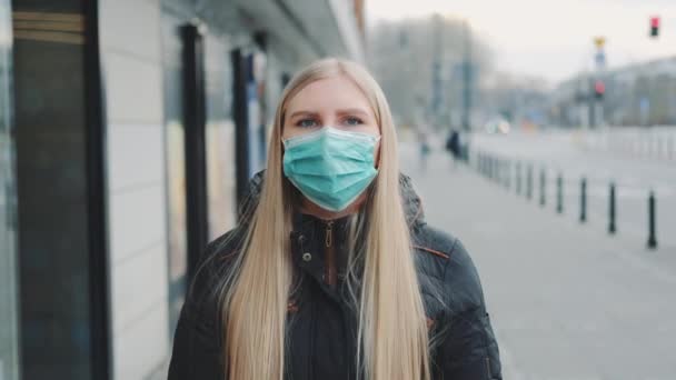 Νεαρή ξανθιά γυναίκα που φοράει προστατευτική ιατρική μάσκα στο δρόμο — Αρχείο Βίντεο