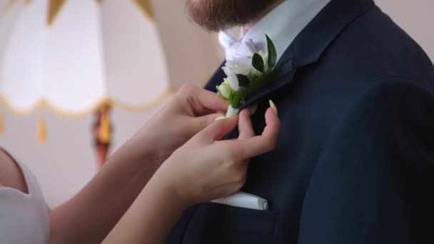 Nevěsta přišpendluje boutonniere k ženichovu oblečení. Malý květ jako svatební dekorace. — Stock video