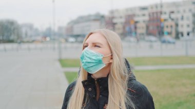 Kadın sokakta yüzüne tıbbi maske takıyor.