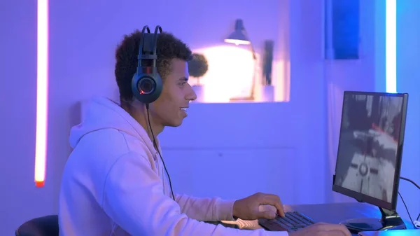 Medium shot of young black gammer in headphones playing in online shooter — Stockfoto