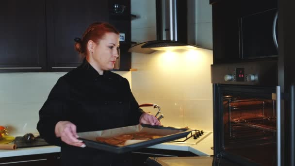 Bäckereiangestellte stellt Backblech mit Plätzchen in den Ofen — Stockvideo