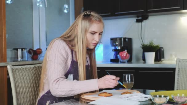 Hermosa mujer pintando galletas dulces con colores especiales de comida en la cocina en casa — Vídeos de Stock