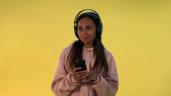 Boldog többnemzetiségű nő hallgat zenét fülhallgató sárga alapon — Stock Fotó