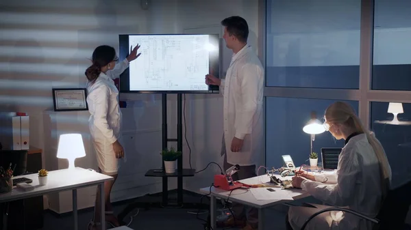 Έξυπνη ομάδα Ηλεκτρολόγων Μηχανικών Ανάπτυξης συζητά κάτι σε μια μεγάλη οθόνη τηλεόρασης στο εργαστήριο — Φωτογραφία Αρχείου