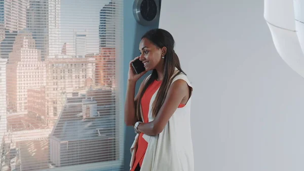 Atractiva modelo africana hablando con alguien en el teléfono inteligente durante el descanso sesión de fotos en el estudio . — Foto de Stock