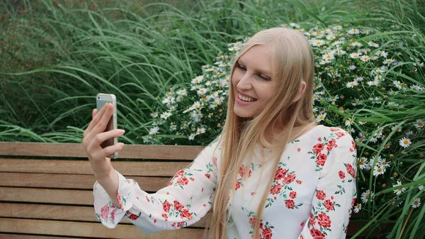 Woman making video call on green roof. Lovely young female using smartphone to make video call while sitting on bench on living roof of huge mall. — Stock Photo, Image