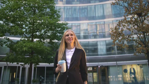Stylish business woman with coffee on street. From below of serious blond executive girl in suit having coffee in paper cup looking away on street.
