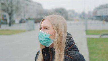 Sokakta yüzüne tıbbi maske takan genç bir kadın.