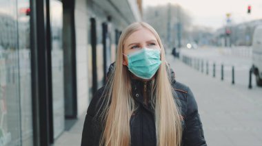 Sokakta koruyucu bir maske takan genç sarışın kadın.