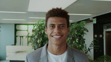 Takım elbiseli yakışıklı siyah adam. Zarif takım elbiseli genç bir Afro-Amerikalı modern ofiste kameraya mutlu bir şekilde gülümsüyor..