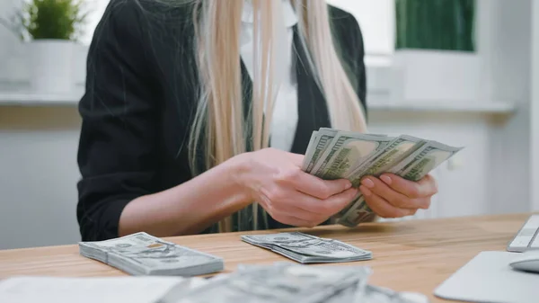 Donna d'affari che conta contanti in mano. Vista ritagliata di femmina in abito elegante seduta alla scrivania di legno e contando grande fascio di banconote in dollari in mano . — Foto Stock