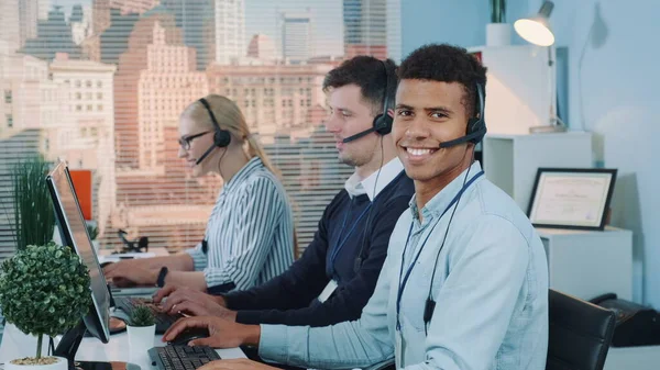 Portrait of smiling mixed-race man taking call in busy call center