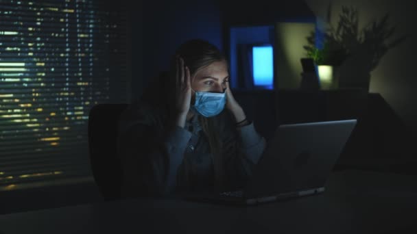 Rädd kvinna i medicinsk mask läser nyheter om coronavirus på laptop i mörker — Stockvideo