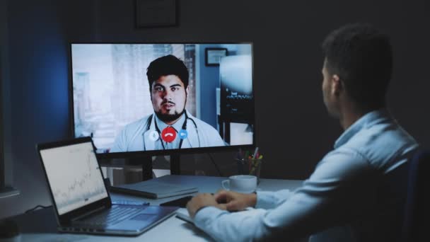 Vue arrière du jeune homme faisant un appel vidéo avec le médecin-chef au sujet de la propagation du coronavirus — Video