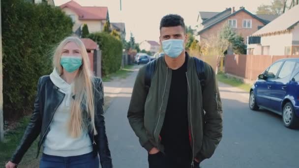 Un homme et une femme multiethniques portant des masques médicaux marchant dans la rue dans un lotissement — Video