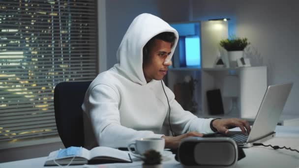 Геймер в білому светрі і з навушниками, які грають в ігри на комп'ютері ввечері — стокове відео