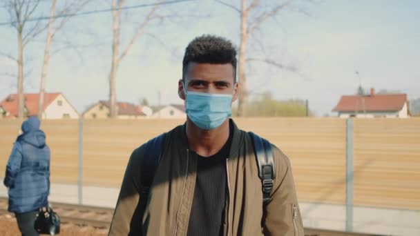 Portret van een jonge Afrikaanse man met een medisch masker die naar de camera kijkt — Stockvideo