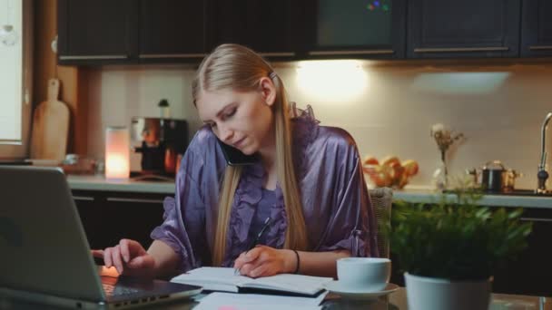 Jonge zakenvrouw die thuis werkt door achter de computer te zitten en met de smartphone te spreken — Stockvideo