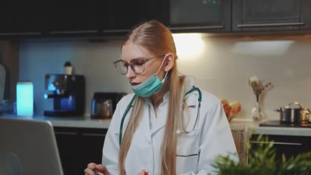 Vrouwelijke arts in medische jurk maken van video bellen naar de patiënt van thuis — Stockvideo
