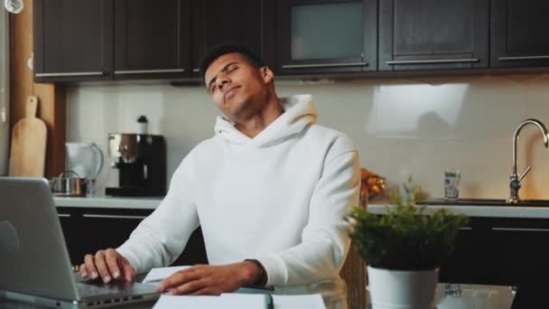 Hombre negro cansado haciendo ejercicio mientras trabaja en la computadora en la cocina en casa — Vídeo de stock