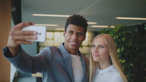 Laughing diverse coworkers taking selfie in office. Cheerful black man with laughing blond woman taking selfie with smartphone in modern office having fun — Stock Photo, Image