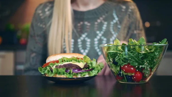 Detailní záběr mladé dámy dává přednost hamburgeru před salátem. — Stock fotografie