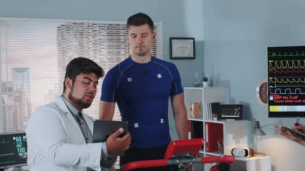 Spor laboratuvarında stres testi: sporcuların EKG verilerini açıklayan tabletli doktor