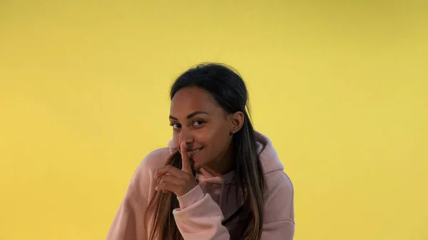 Beautiful mixed-race woman making a hush gesture on yellow background. — Stock Photo, Image