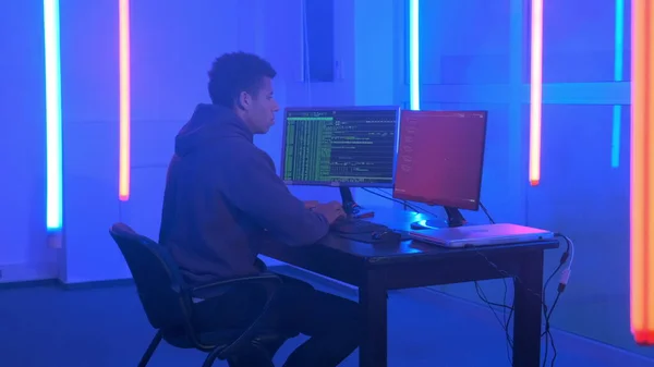 Young african man writing hacker programs in dark room with neon lights — Stockfoto