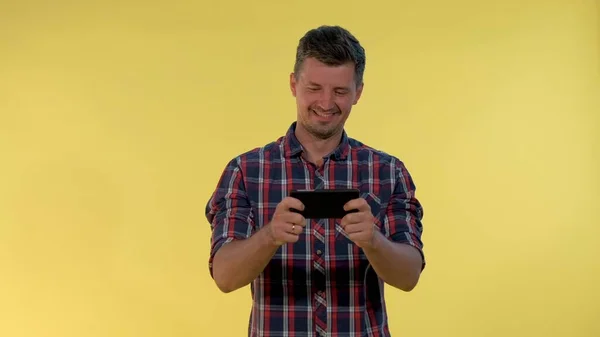 Positive young man enjoy playing online game on smartphone on yellow background — Stock Photo, Image