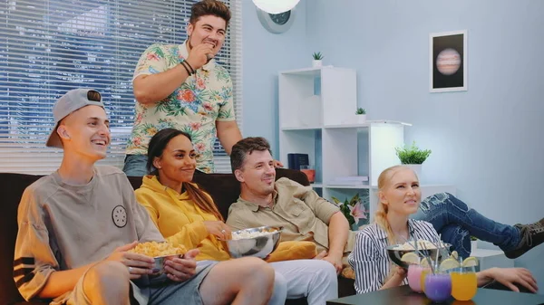 Alegre compañía viendo la televisión, comiendo bocadillos y disfrutando del tiempo juntos —  Fotos de Stock