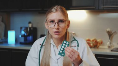 Hastaya video çağrısı: tıp önlüklü kadın doktor kameraya bakıyor ve nasıl ilaç alınacağını anlatıyor.