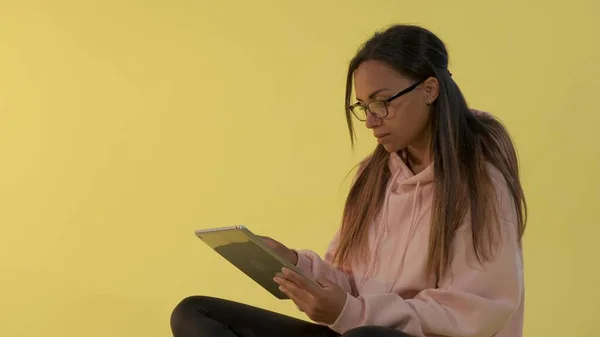 Mujer negra en gafas graduadas trabajando sobre tableta sobre fondo amarillo . — Foto de Stock