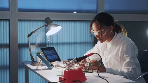 Nahaufnahme eines afrikanisch-amerikanischen Elektronikingenieurs in Schutzbrille, der das Motherboard mit einem Multimeter-Tester überprüft — Stockfoto