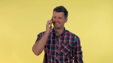 Hoş görünümlü genç adam sarı arka planda akıllı telefonla biriyle konuşuyor..