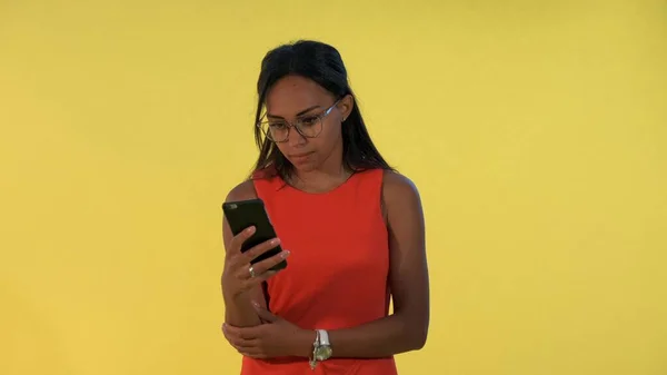 Multiracial vacker kvinna tittar förvånad över smartphone på gul bakgrund. — Stockfoto