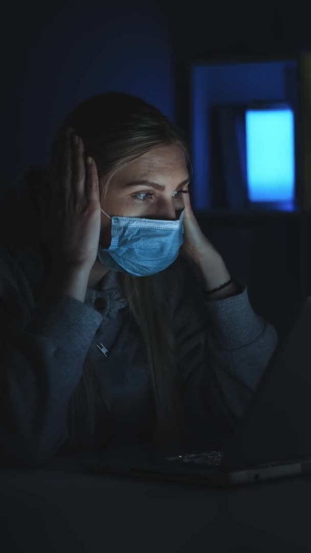 Τρομαγμένη γυναίκα με ιατρική μάσκα που διαβάζει νέα για τον κορωναϊό στο λάπτοπ στο σκοτάδι. — Αρχείο Βίντεο