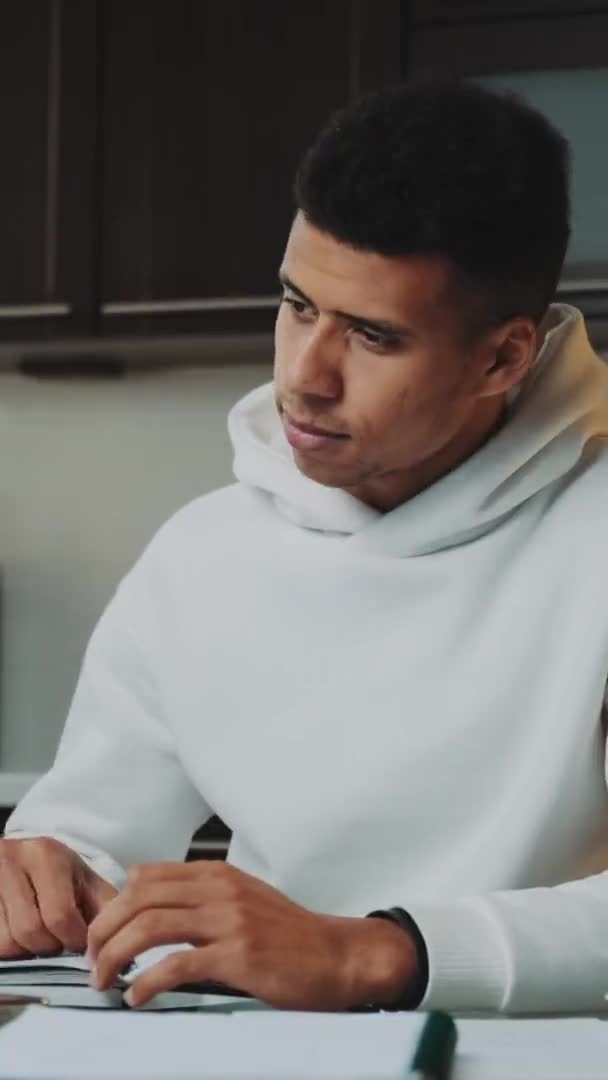 Zwart man in wit hoodie werken thuis op de computer — Stockvideo