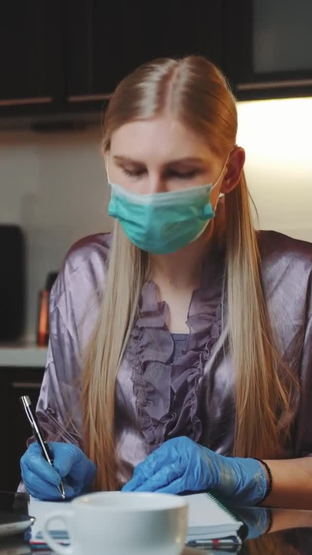 Mujer rubia en máscara médica y guantes trabajando en casa y sonriendo al monitor — Vídeo de stock