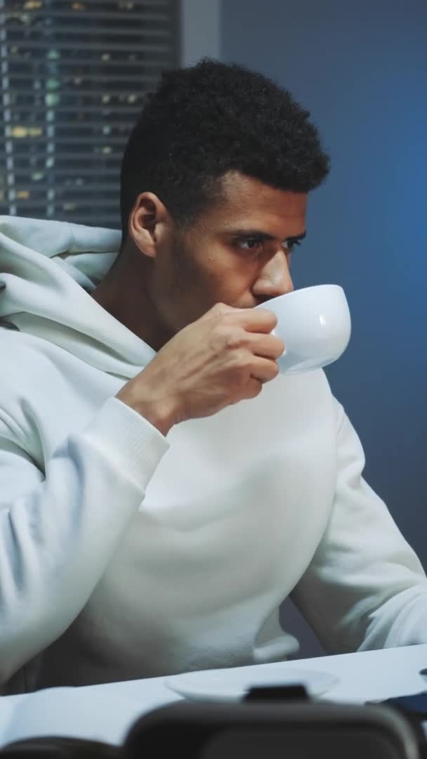 Jóképű multiracionális férfi iszik egy csésze kávét és éjjel számítógépen dolgozik. — Stock videók