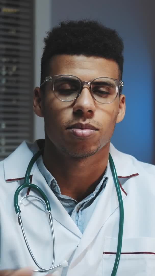 Close-up of young african doctor looking to the camera and telling about something in the evening — Stock Video