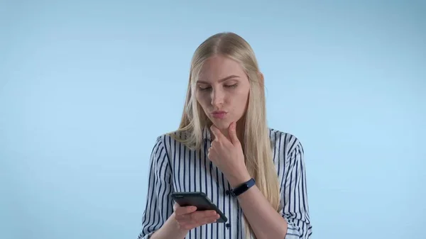 Inteligentna młoda kobieta patrzy na smartfona i zaczyna planować coś na niebieskim tle. — Zdjęcie stockowe