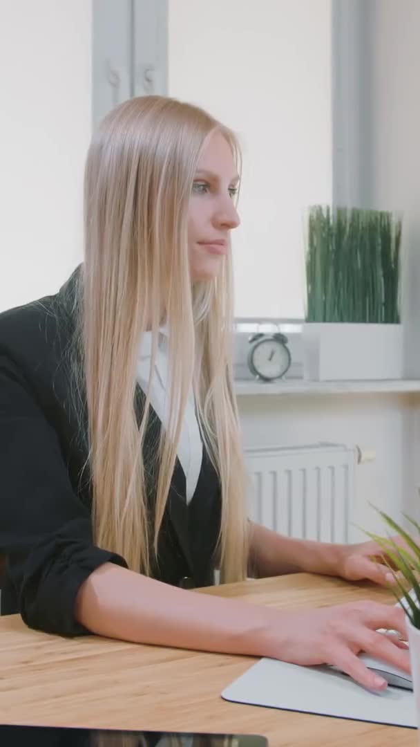 Uśmiechnięta kobieta pracująca na komputerze w biurze. Piękna młoda blondynka siedzi w miejscu pracy z komputerem i trzyma rękę na myszy patrząc w kamerę i uśmiechając się. — Wideo stockowe