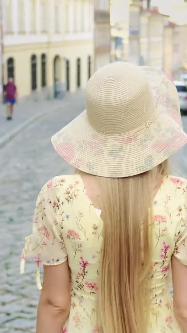 Mosolygó fiatal nő sétál az utcán. Vidám, fehér kalapos lány, aki a kamerába néz, miközben a városban sétál.. — Stock videók
