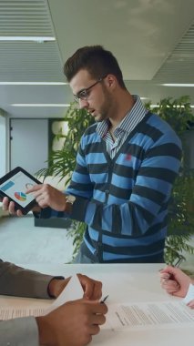 Kağıtları ve tabletleri olan çok ırklı iş arkadaşları. Masada çalışan, gazete okuyan ve tablet kullanan siyahi bir adamın yan görüntüsü..